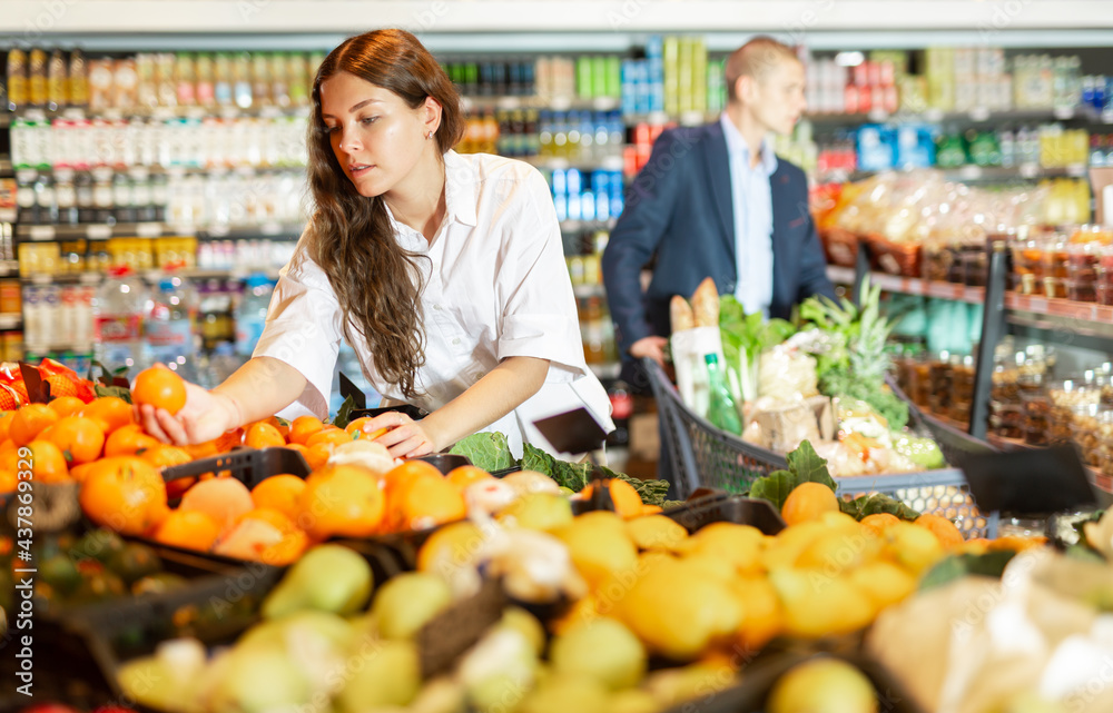 Female shopper picks ripe oranges on grocery store shelves