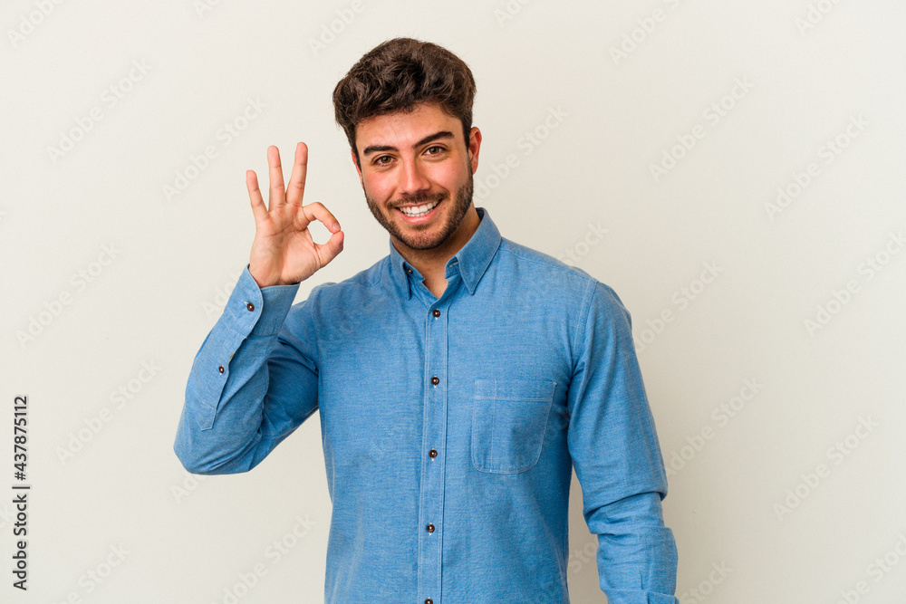 Young caucasian man isolated on white background winks an eye and holds an okay gesture with hand. Young caucasian man isolated on white background winks an eye and holds an okay gesture with hand.