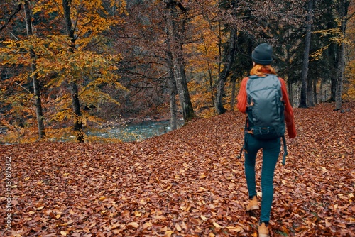 woman tourist with a backpack walking in the park with fallen leaves in autumn in nature