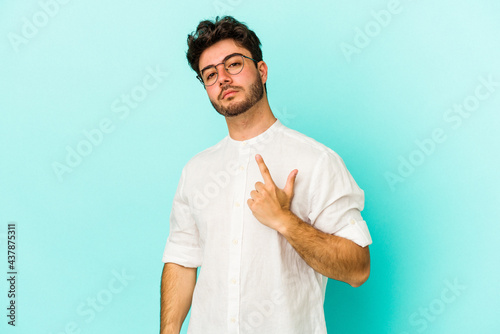 Young caucasian man isolated on blue background pointing with finger at you as if inviting come closer.