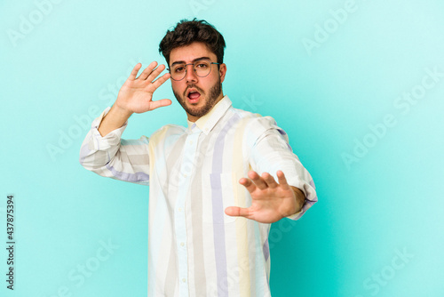 Young caucasian man isolated on blue background being shocked due to an imminent danger