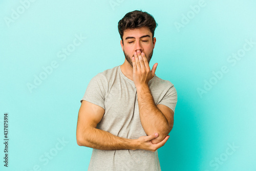 Tableau sur toile Young caucasian man isolated on blue background yawning showing a tired gesture covering mouth with hand