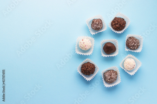 Tasty ball-shaped chocolate candies packed in small paper baskets on blue background. Romantic valentine's day day dessert. Delicious sweet. Minimal style. Flat lay, top view with copy scape.