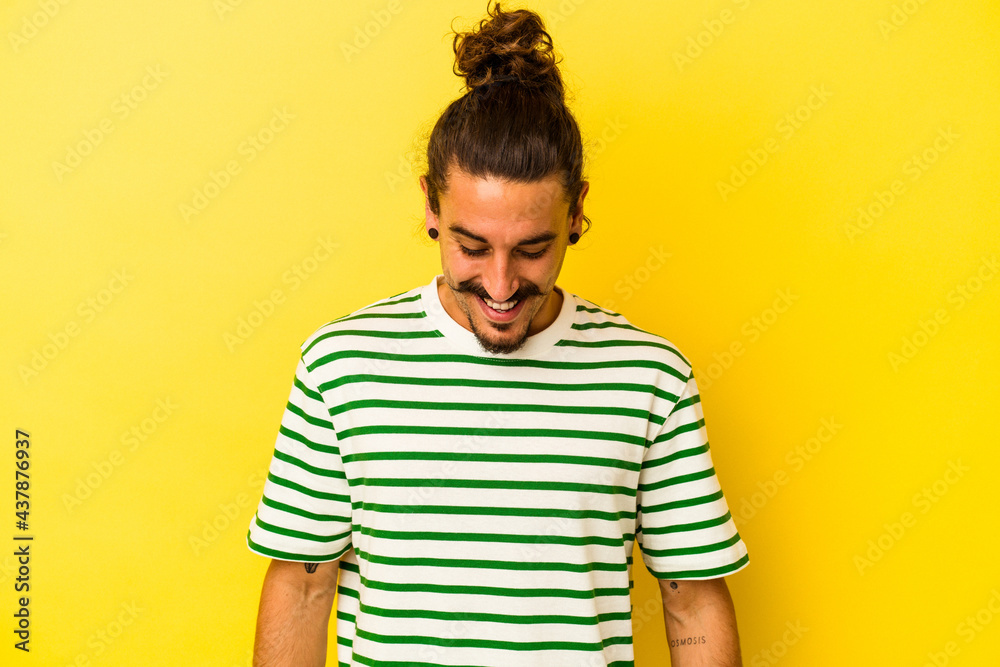 Young caucasian man with long hair isolated on yellow background laughs and closes eyes, feels relaxed and happy. Young caucasian man with long hair isolated on yellow background laughs and closes eyes, feels relaxed and happy.