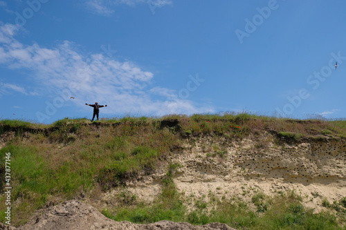 Scene with a male silhouette on top of a hill. Flying swift birds that have nests in the sandy slope.