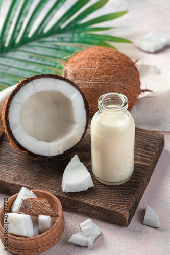 Coconut milk, a healthy drink made from coconut on a light pink background with palm leaves and coconuts. Side view, vertical.