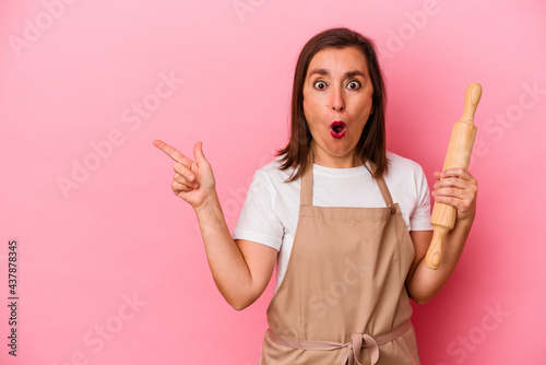 Middle age pastry chef woman isolated on pink background pointing to the side