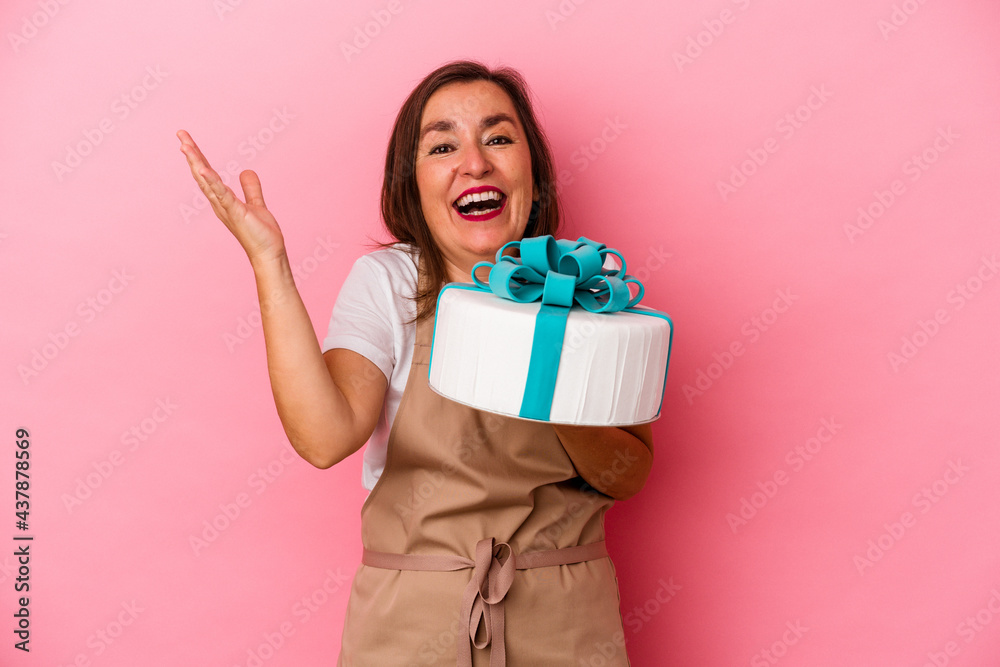 Middle aged pastry chef woman holding a cake isolated on blue background receiving a pleasant surprise, excited and raising hands. Middle aged pastry chef woman holding a cake isolated on blue background receiving a pleasant surprise, excited and raising hands.