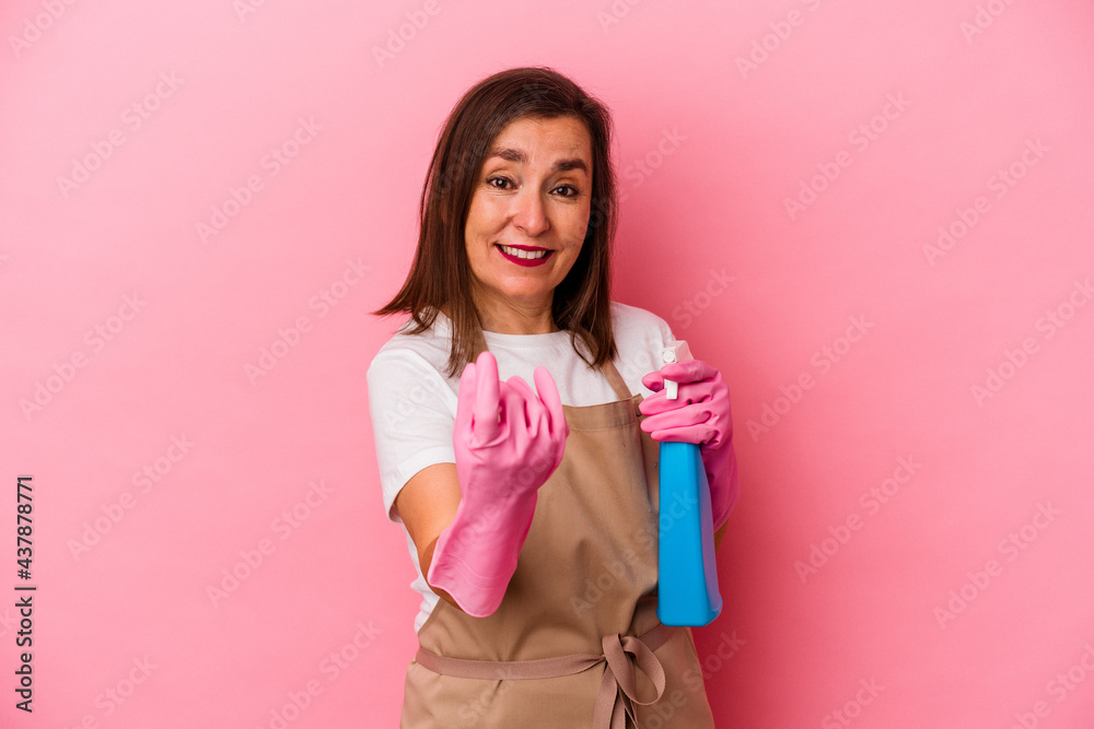 Middle age caucasian woman cleaning home isolated on pink background pointing with finger at you as if inviting come closer.