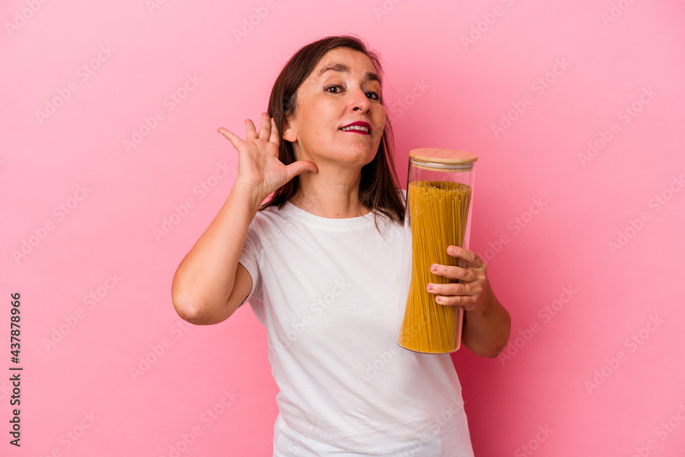 Middle age caucasian woman holding a pasta jar isolated on pink background trying to listening a gossip. Middle age caucasian woman holding a pasta jar isolated on pink background trying to listening a gossip.
