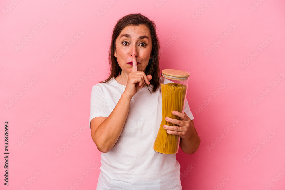Middle age caucasian woman holding a pasta jar isolated on pink background keeping a secret or asking for silence.