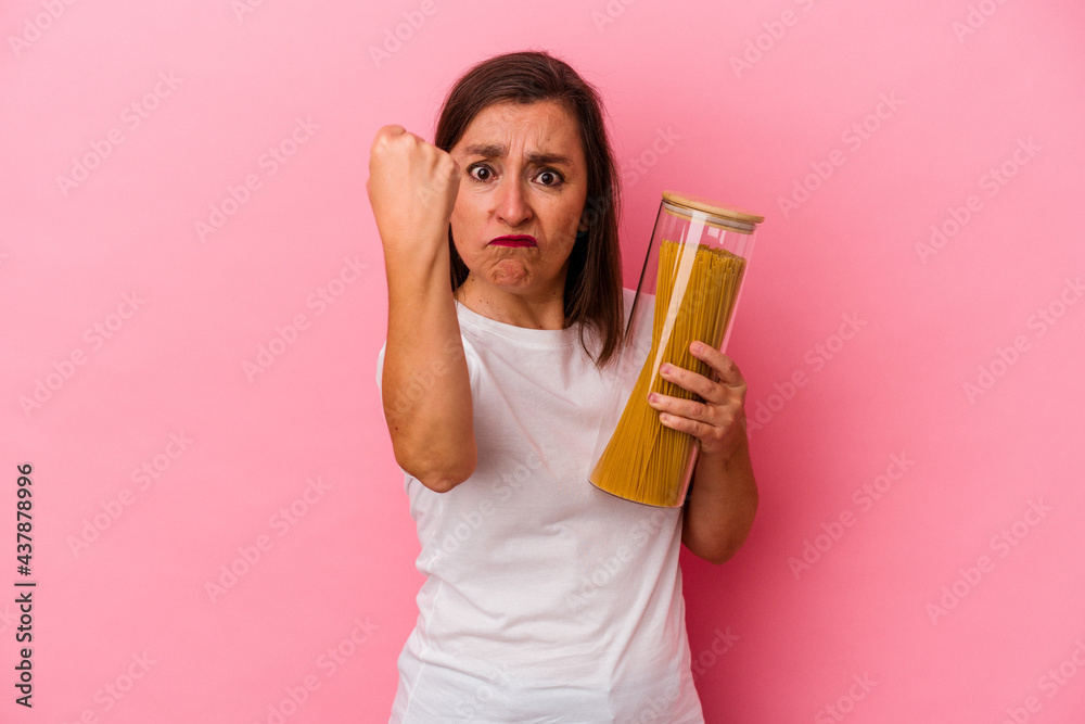 Middle age caucasian woman holding a pasta jar isolated on pink background showing fist to camera, aggressive facial expression. Middle age caucasian woman holding a pasta jar isolated on pink background showing fist to camera, aggressive facial expression.