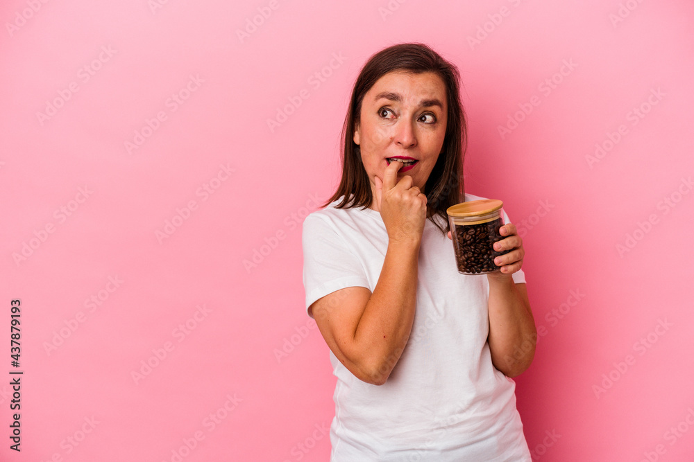 Middle age caucasian woman holding a coffee jar isolated on pink background relaxed thinking about something looking at a copy space. Middle age caucasian woman holding a coffee jar isolated on pink background relaxed thinking about something looking at a copy space.