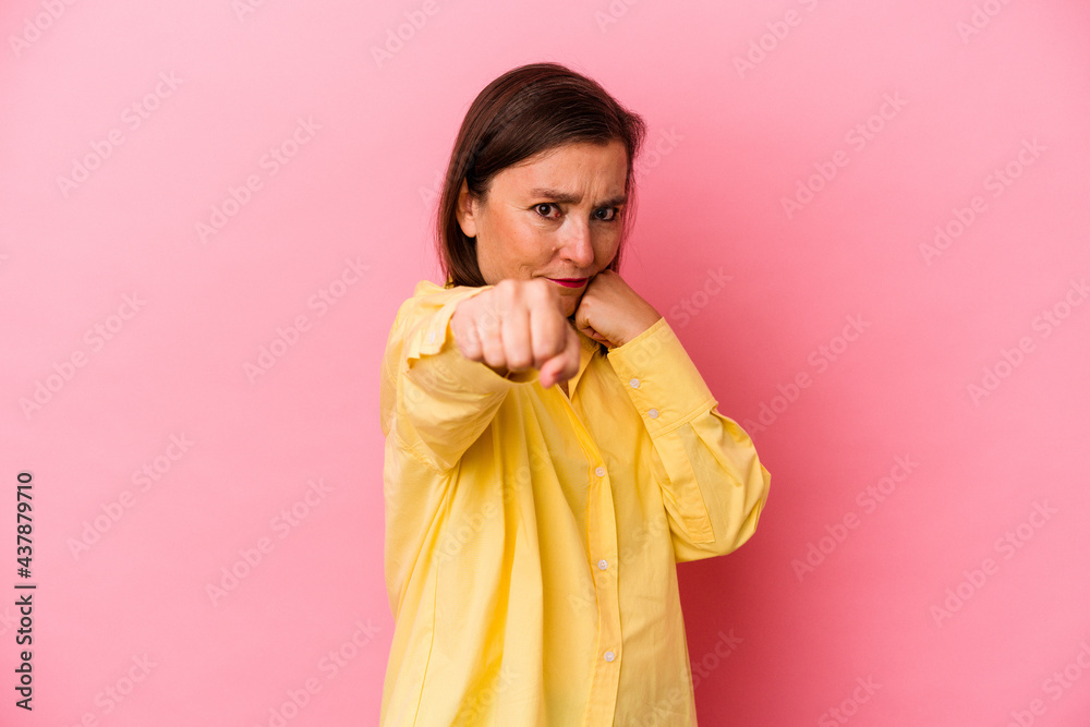 Middle age caucasian woman isolated on pink background throwing a punch, anger, fighting due to an argument, boxing.