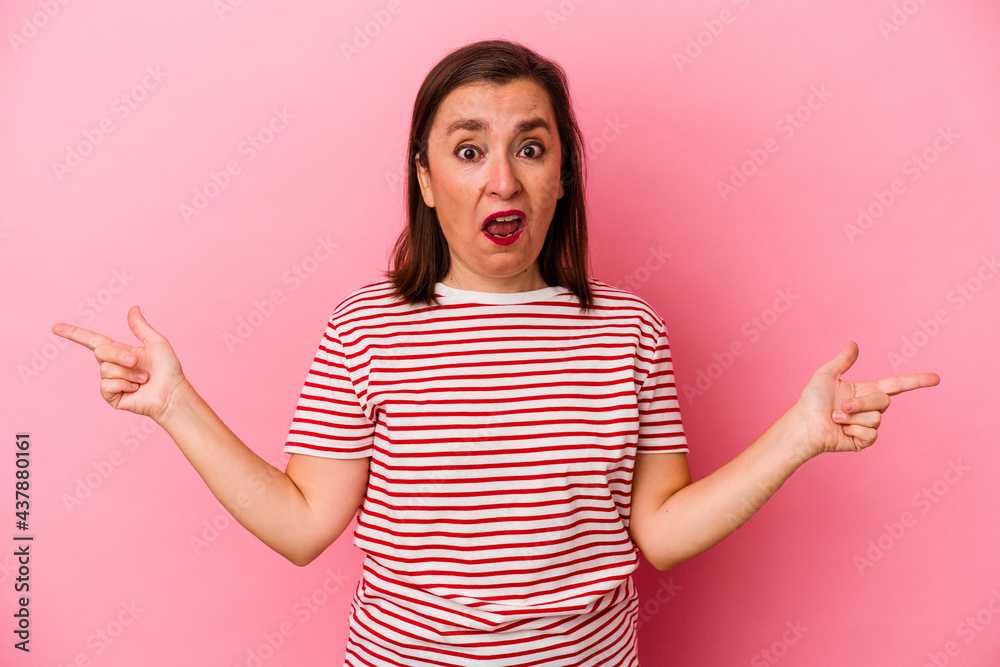 Middle age caucasian woman isolated on pink background pointing to different copy spaces, choosing one of them, showing with finger.