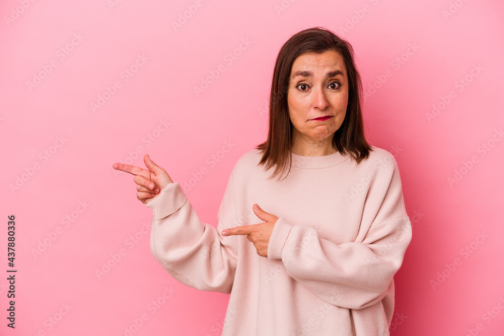 Middle age caucasian woman isolated on pink background shocked pointing with index fingers to a copy space. Middle age caucasian woman isolated on pink background shocked pointing with index fingers to a copy space.