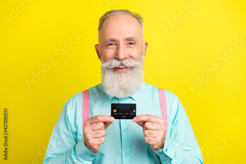 Photo of optimistic elder man hold card wear blue shirt suspenders isolated on yellow color background © deagreez