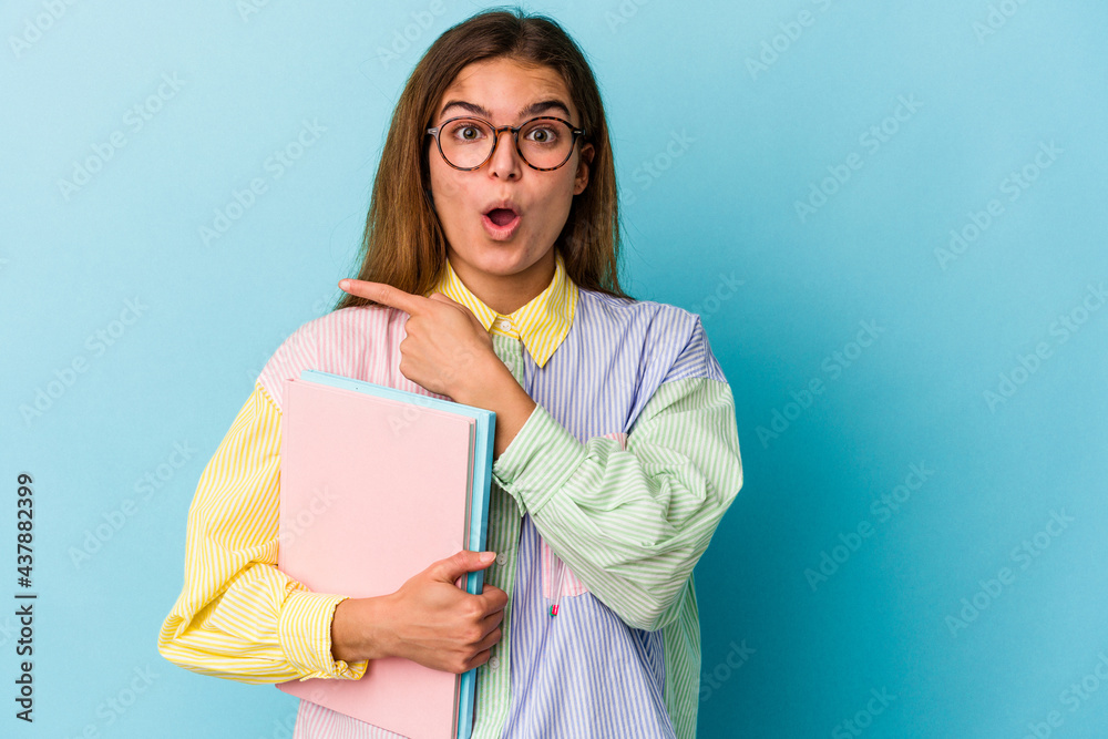 Fototapeta premium Young caucasian student woman holding books isolated on blue background pointing to the side