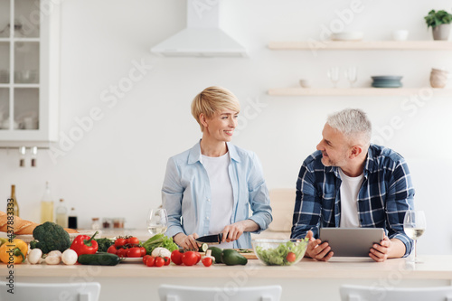 Happy asian family couple cooking food, vegetable salad in kitchen together at home with device