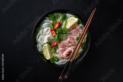 Pho Bo vietnamese soup with beef and rice noodles on a black background, top view