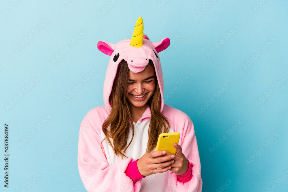 Young caucasian woman wearing a unicorn pajama holding a mobile phone isolated on blue background Young caucasian woman wearing a unicorn pajama holding a mobile phone isolated on blue background