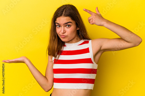 Young caucasian woman isolated on yellow background holding and showing a product on hand.