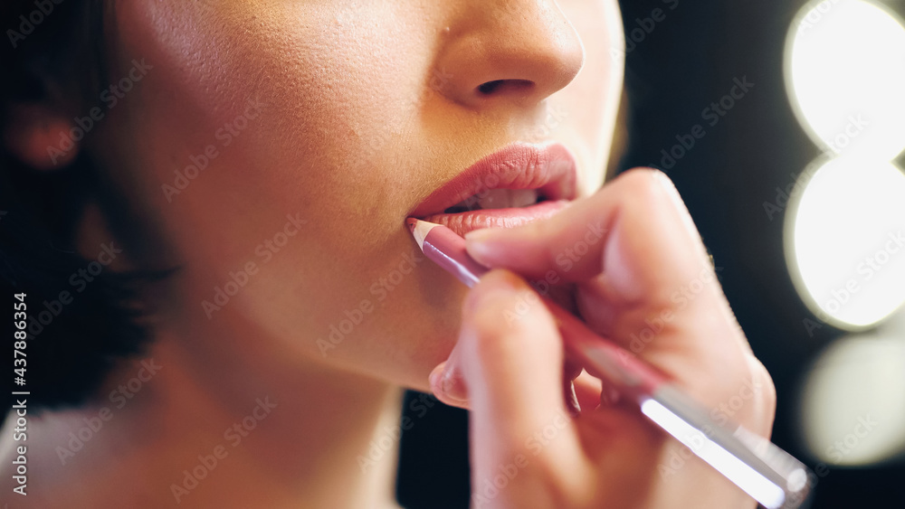 cropped view of blurred makeup artist applying lip pencil on lips of woman