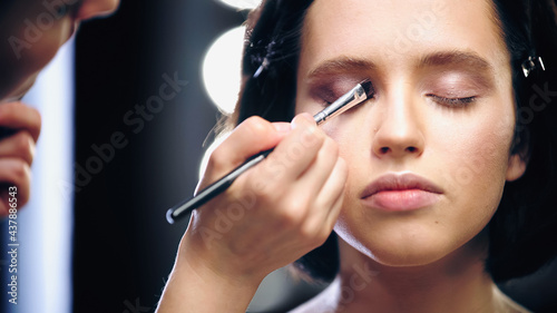 makeup artist applying eye shadow with cosmetic brush on eyelids of model