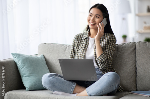Pretty young woman having phone conversation, using laptop