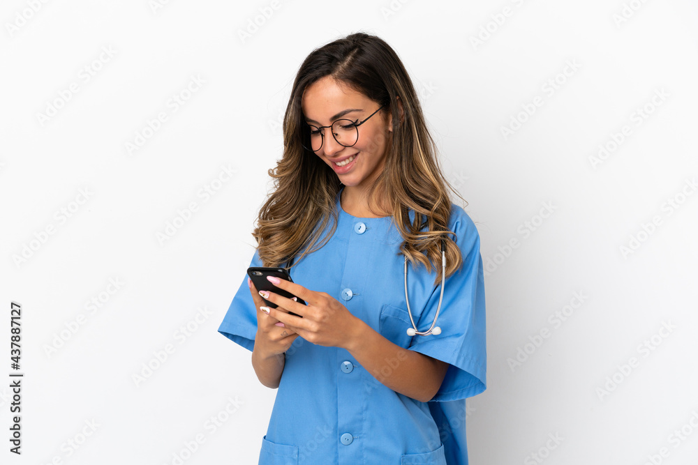 Young surgeon doctor woman over isolated white wall sending a message with the mobile Young surgeon doctor woman over isolated white wall sending a message with the mobile