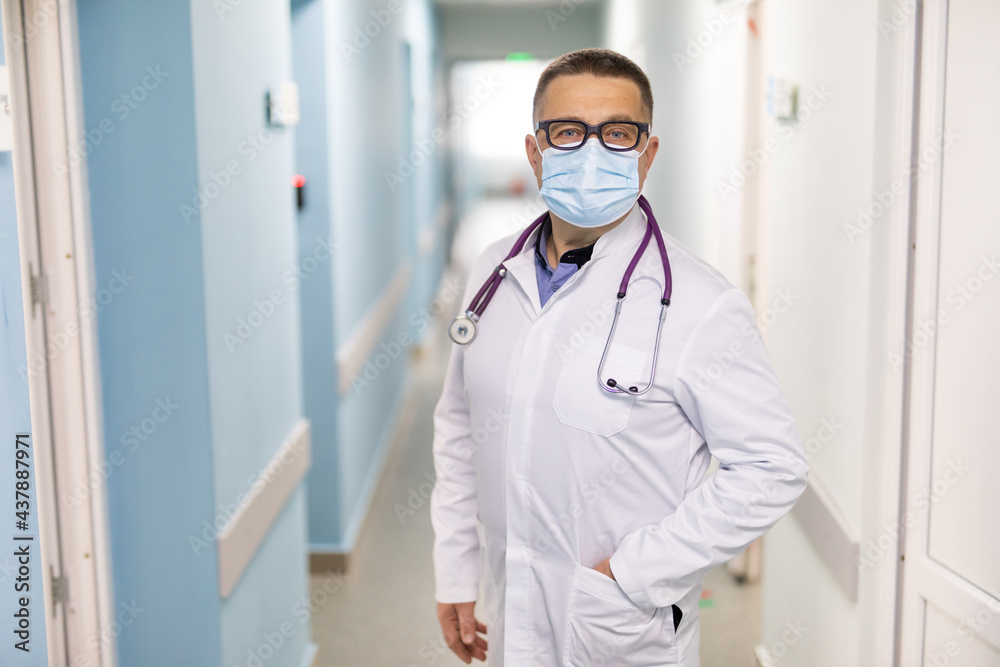 Portrait of male doctor wearing face mask standing in hospital corridor. medicine, health and healthcare services during coronavirus covid 19 pandemic. Portrait of male doctor wearing face mask standing in hospital corridor. medicine, health and healthcare services during coronavirus covid 19 pandemic.