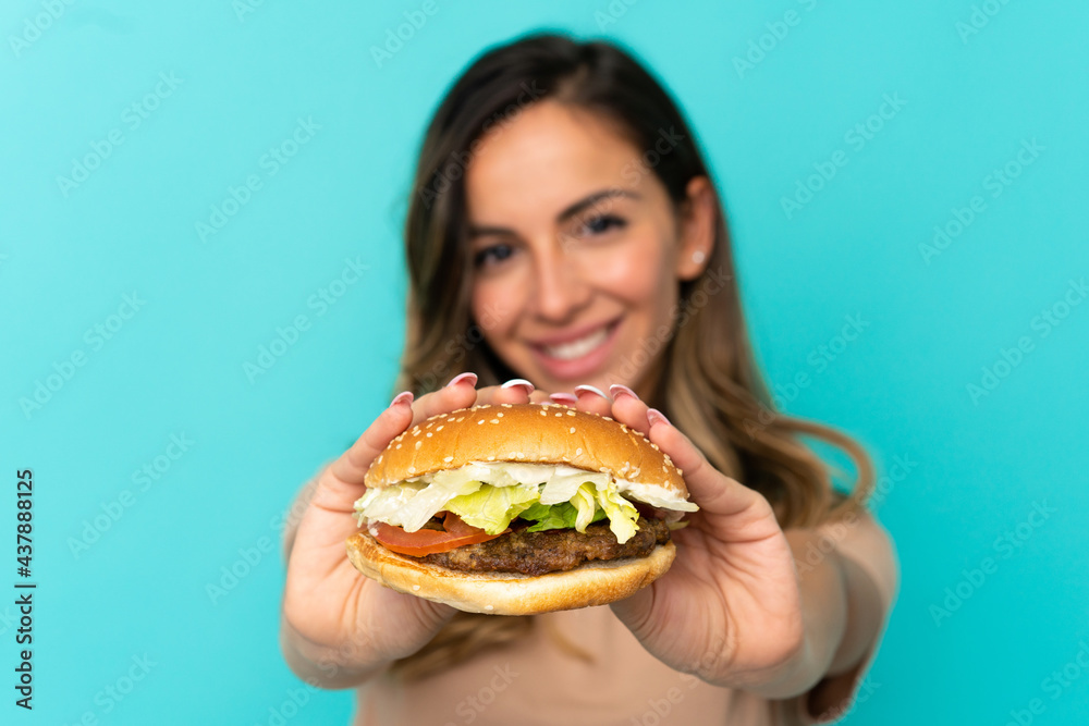 Young woman holding a burger over isolated background Young woman holding a burger over isolated background