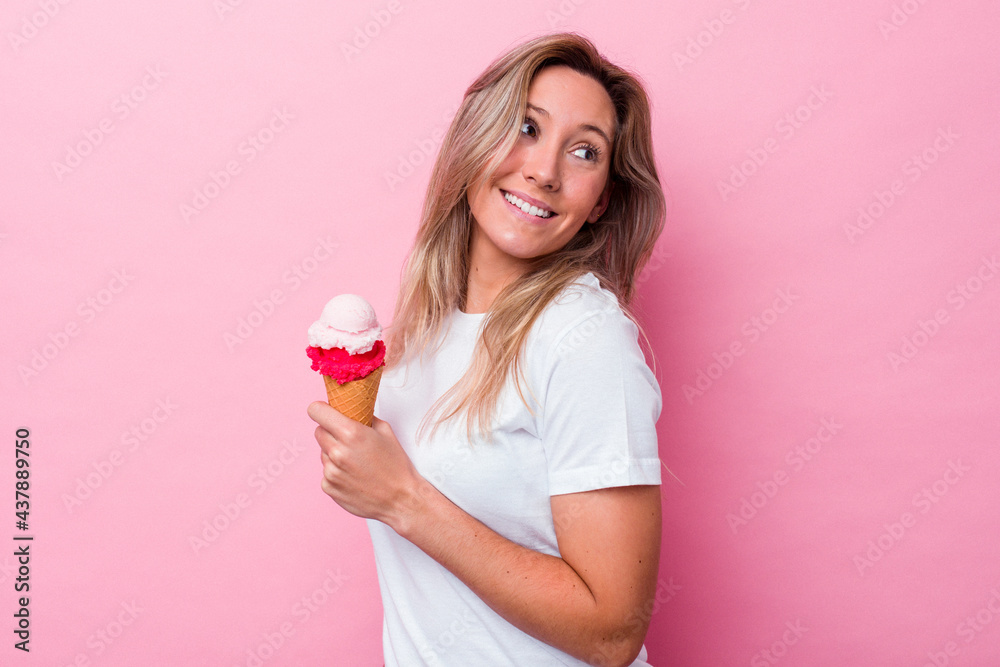 Young australian woman holding an ice cream isolated on pink background looks aside smiling, cheerful and pleasant. Young australian woman holding an ice cream isolated on pink background looks aside smiling, cheerful and pleasant.