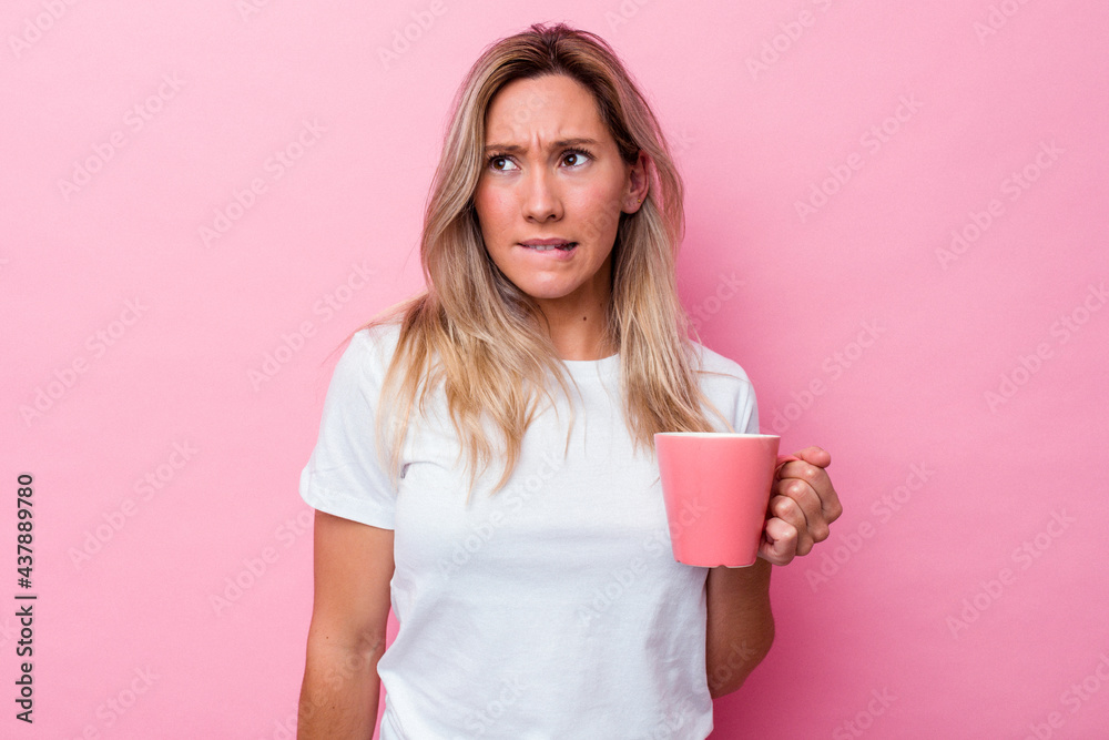 Young australian woman holding a pink mug isolated on pink background confused, feels doubtful and unsure. Young australian woman holding a pink mug isolated on pink background confused, feels doubtful and unsure.