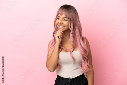 Young mixed race woman with pink hair isolated on pink background looking to the side and smiling