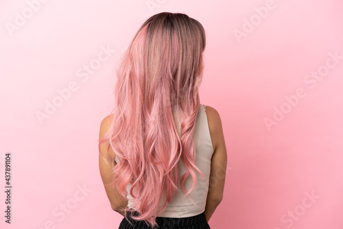 Young mixed race woman with pink hair isolated on pink background in back position and looking side photo