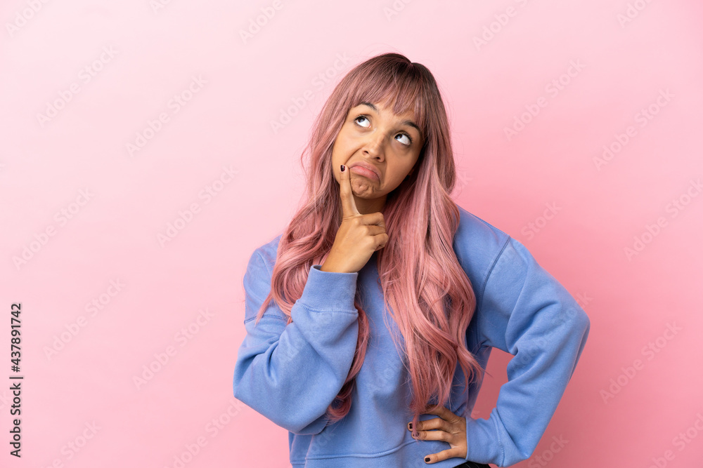 Young mixed race woman with pink hair isolated on pink background having doubts while looking up Young mixed race woman with pink hair isolated on pink background having doubts while looking up