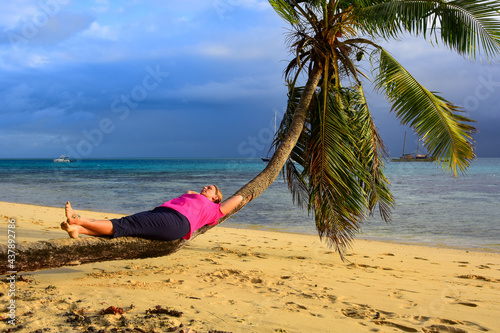 Woman relaxing on sideways growing palm near the sea on a tropical island