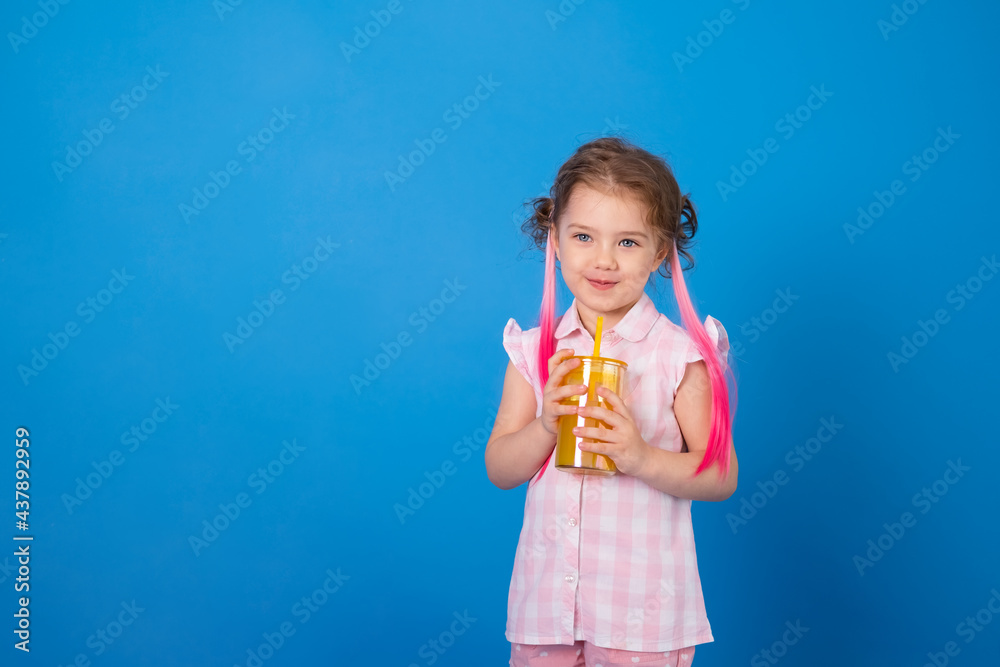 Funny child girl in pink clothes smiling holding glass of orange juice on blue background Funny child girl in pink clothes smiling holding glass of orange juice on blue background