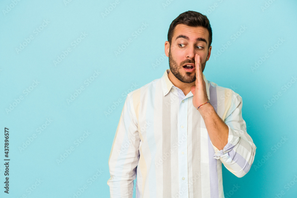 Young caucasian man isolated on blue background is saying a secret hot braking news and looking aside Young caucasian man isolated on blue background is saying a secret hot braking news and looking aside