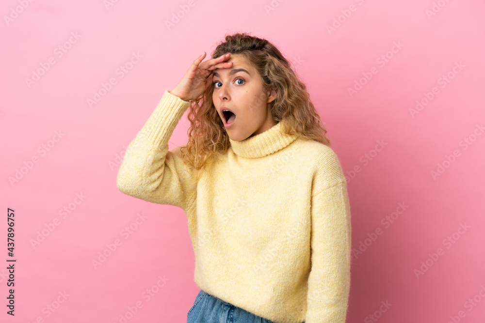 Young blonde woman isolated on pink background doing surprise gesture while looking to the side Young blonde woman isolated on pink background doing surprise gesture while looking to the side