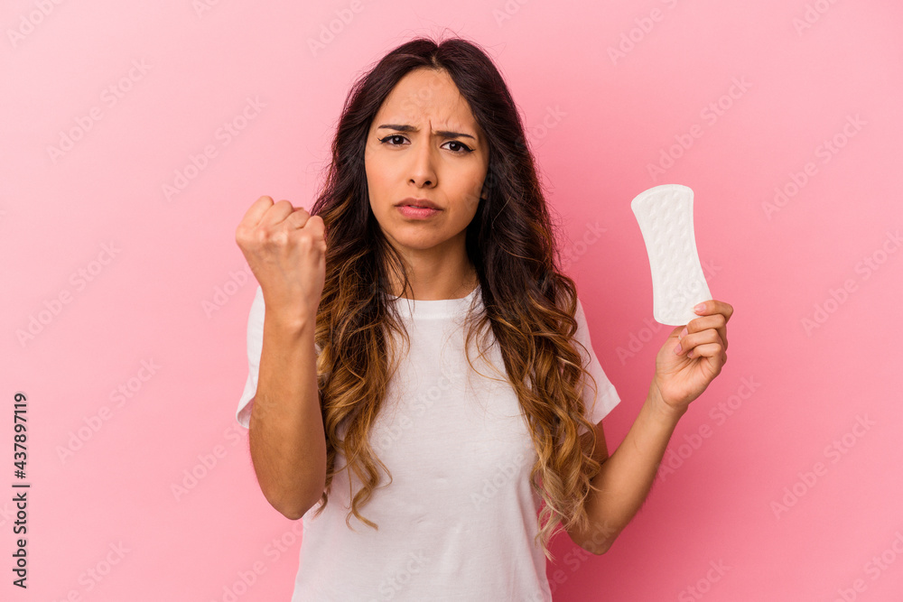 Young mexican woman holding a compress isolated on pink background showing fist to camera, aggressive facial expression. Young mexican woman holding a compress isolated on pink background showing fist to camera, aggressive facial expression.