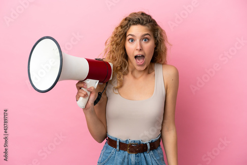 Young blonde woman isolated on pink background holding a megaphone and with surprise expression