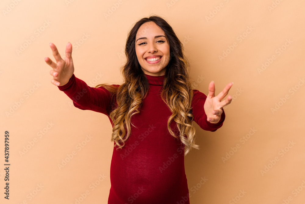 Young mexican pregnant woman isolated on beige background feels confident giving a hug to the camera. Young mexican pregnant woman isolated on beige background feels confident giving a hug to the camera.
