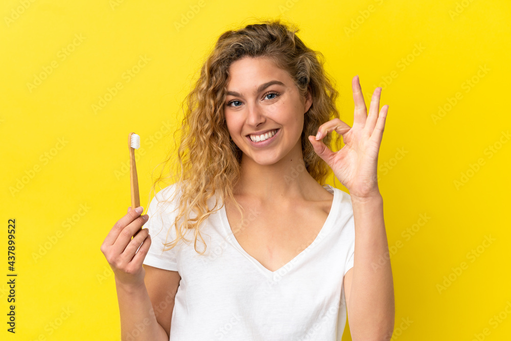 Young caucasian woman holding a brushing teeth isolated on yellow background showing ok sign with fingers Young caucasian woman holding a brushing teeth isolated on yellow background showing ok sign with fingers