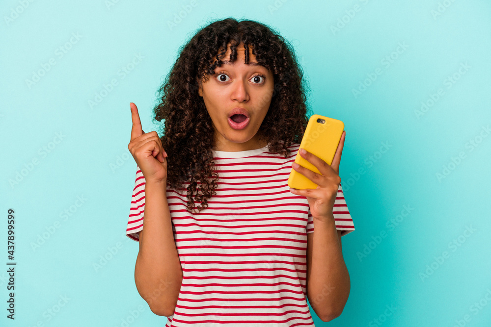 Young mixed race woman holding a mobile phone isolated on blue background having an idea, inspiration concept. Young mixed race woman holding a mobile phone isolated on blue background having an idea, inspiration concept.