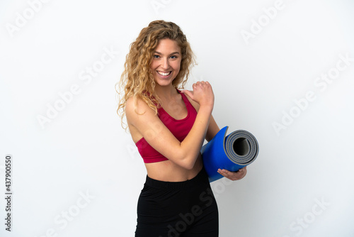 Young sport blonde woman going to yoga classes while holding a mat isolated on white background proud and self-satisfied