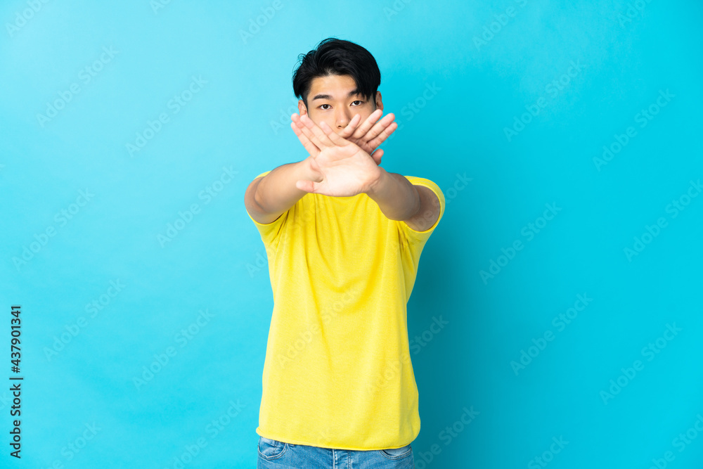 Young Chinese man isolated on blue background making stop gesture with her hand to stop an act