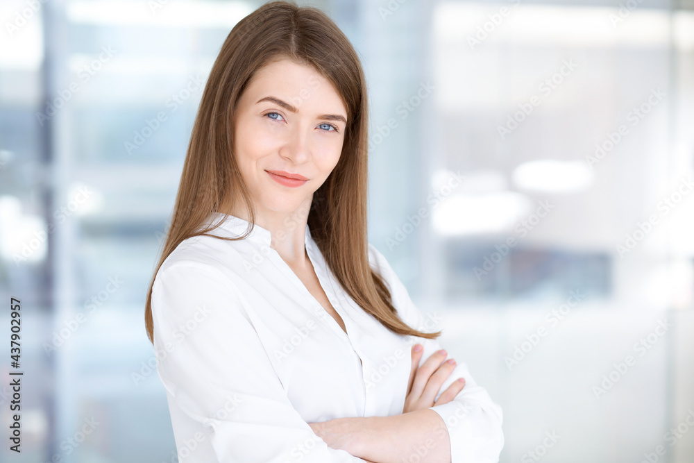 Beautiful female specialist with arms crossed standing in modern office and smiling charmingly. Working on design, data analysis, plan strategy. Business people concept