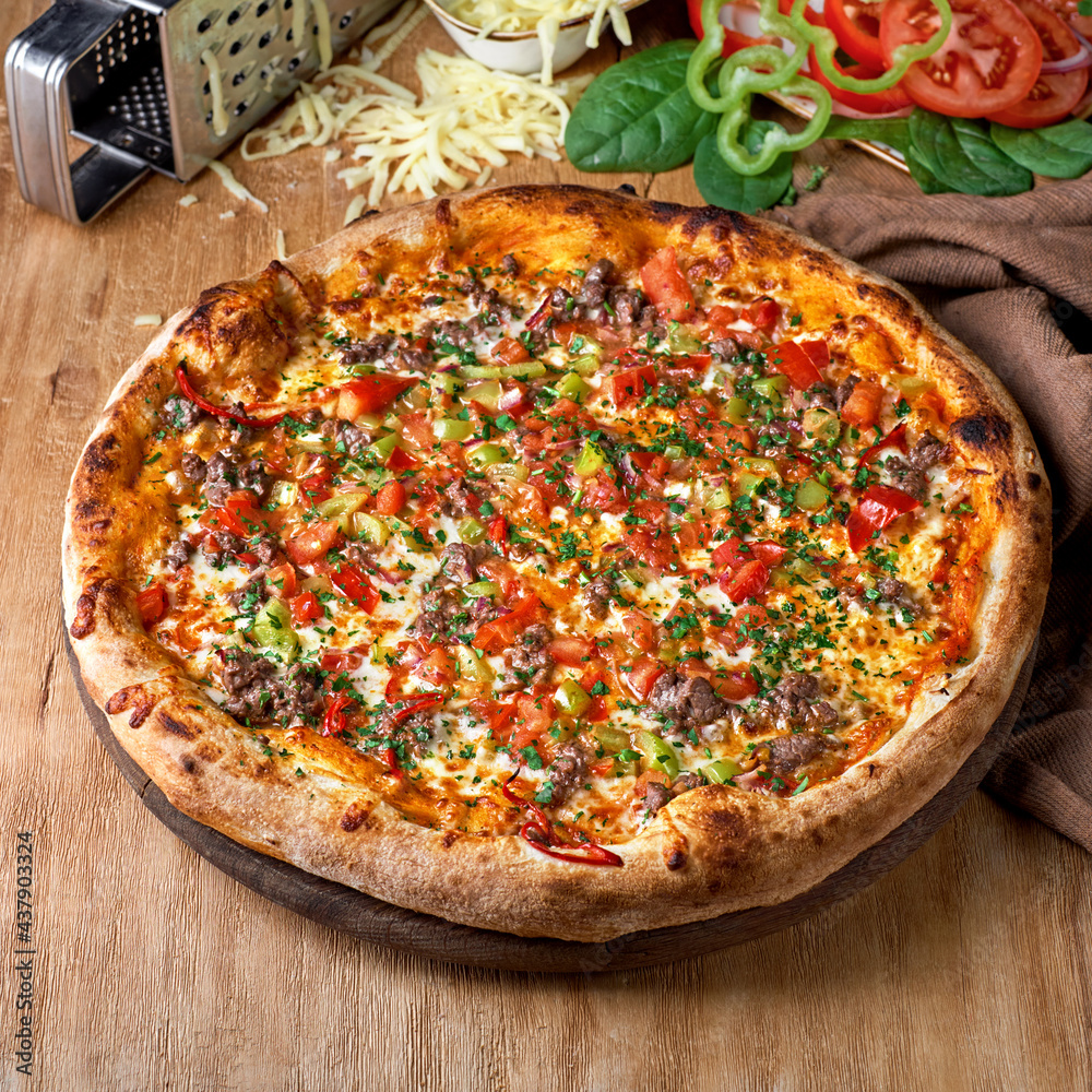 Delicious pizza base topped with tomato sauce, beef, tomato, red onion and cheese on wooden background.